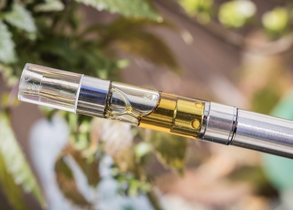 Cannabis vape cartridge filled with amber-colored marijuana oil displayed upright on a clean surface.